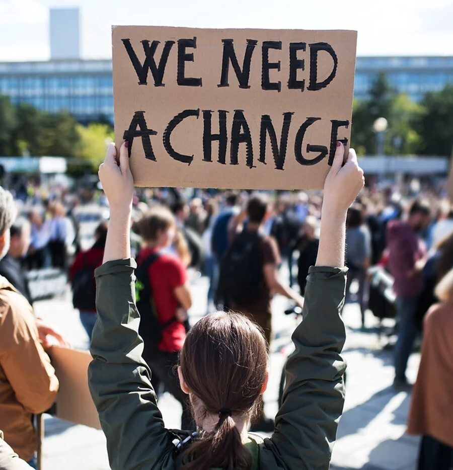 Woman holding up sign that says We Need a Change